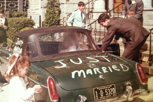 Couple gets into a green little green car with Just Married painted on the windows.